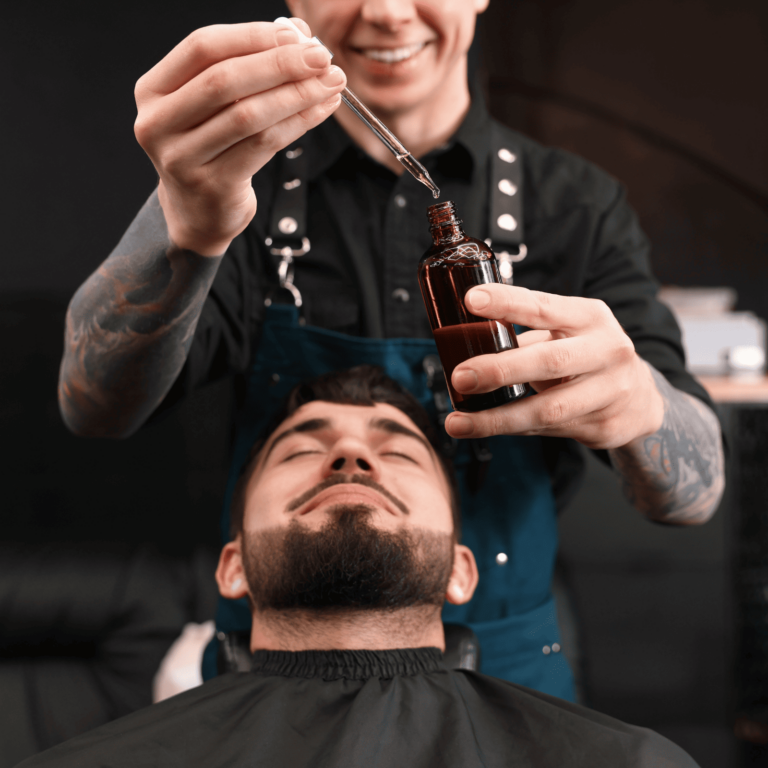 A barber applies beard oil to a customer's beard using a dropper in a barbershop.