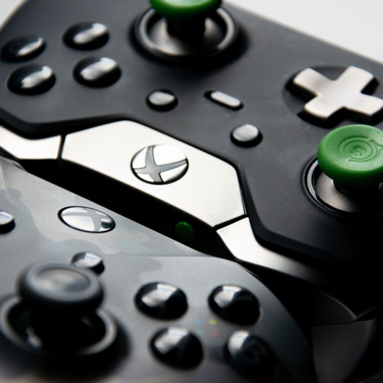 Close-up of two Xbox controllers, featuring black and silver designs with green thumb grips on the joysticks.