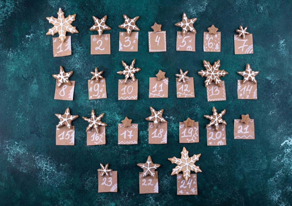 An advent calendar for men featuring numbered brown cards, each adorned with a star-shaped cookie topped with white icing. These stylish cards are arranged in four neat rows against a dark green backdrop, bringing festive charm to the holiday season.