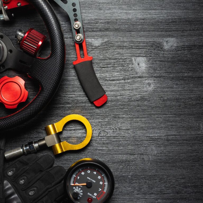 A collection of automotive tools and accessories, including a steering wheel, gauge, and glove, on a dark wooden surface.