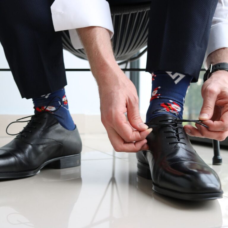 A person wearing blue patterned socks and suit pants is tying black dress shoe laces.