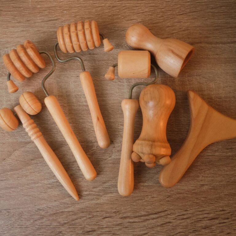Wooden massage tools on a wooden surface, featuring rollers, mallets, and a contour tool.