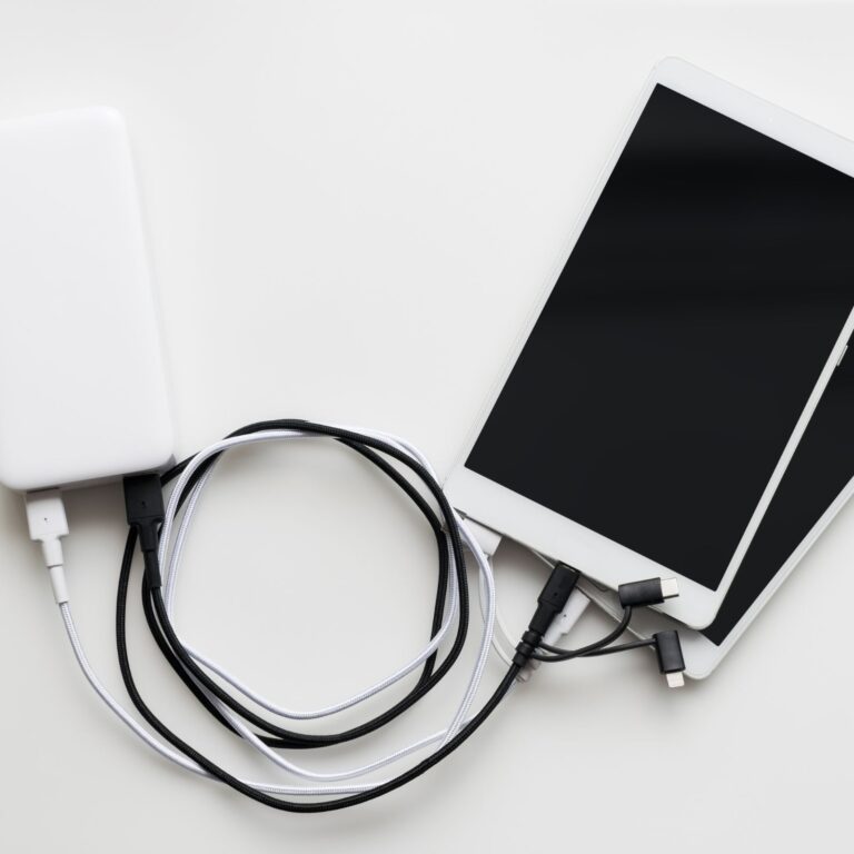 A tablet connected to a power bank with multiple charging cables on a white surface.