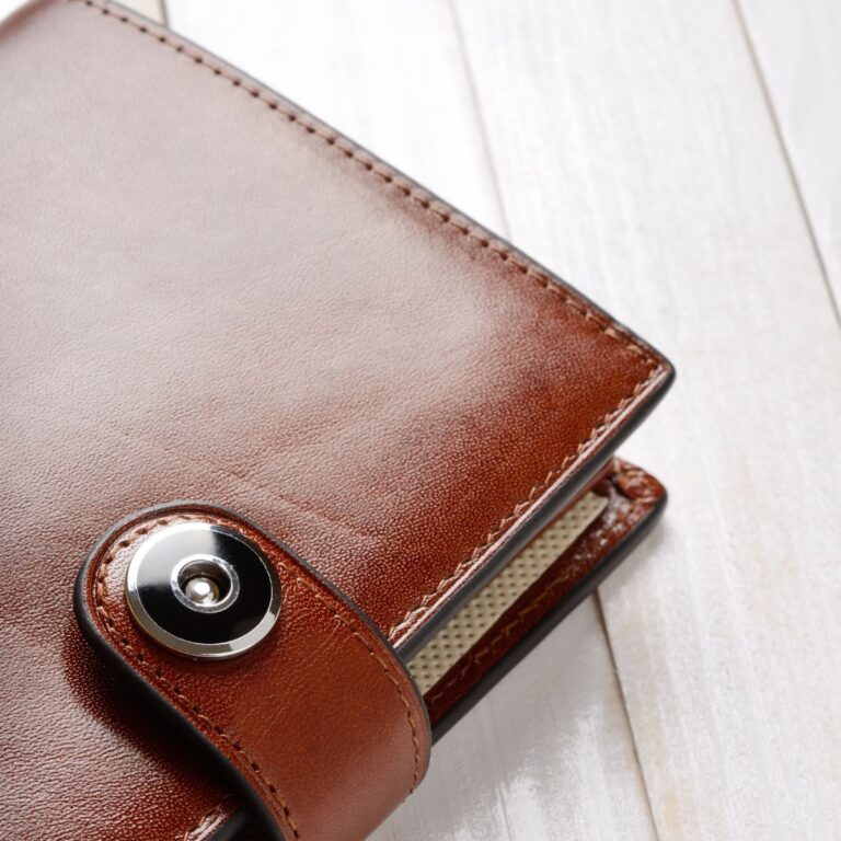Close-up of a brown leather men's wallet with a metal button clasp on a light wooden surface.