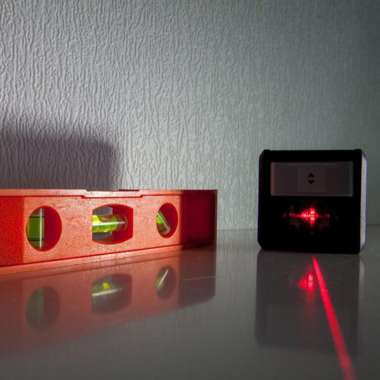 A red laser level projects a beam onto a wall, alongside a red spirit level on a reflective surface, showcasing the precision and reliability of essential garage gadgets.