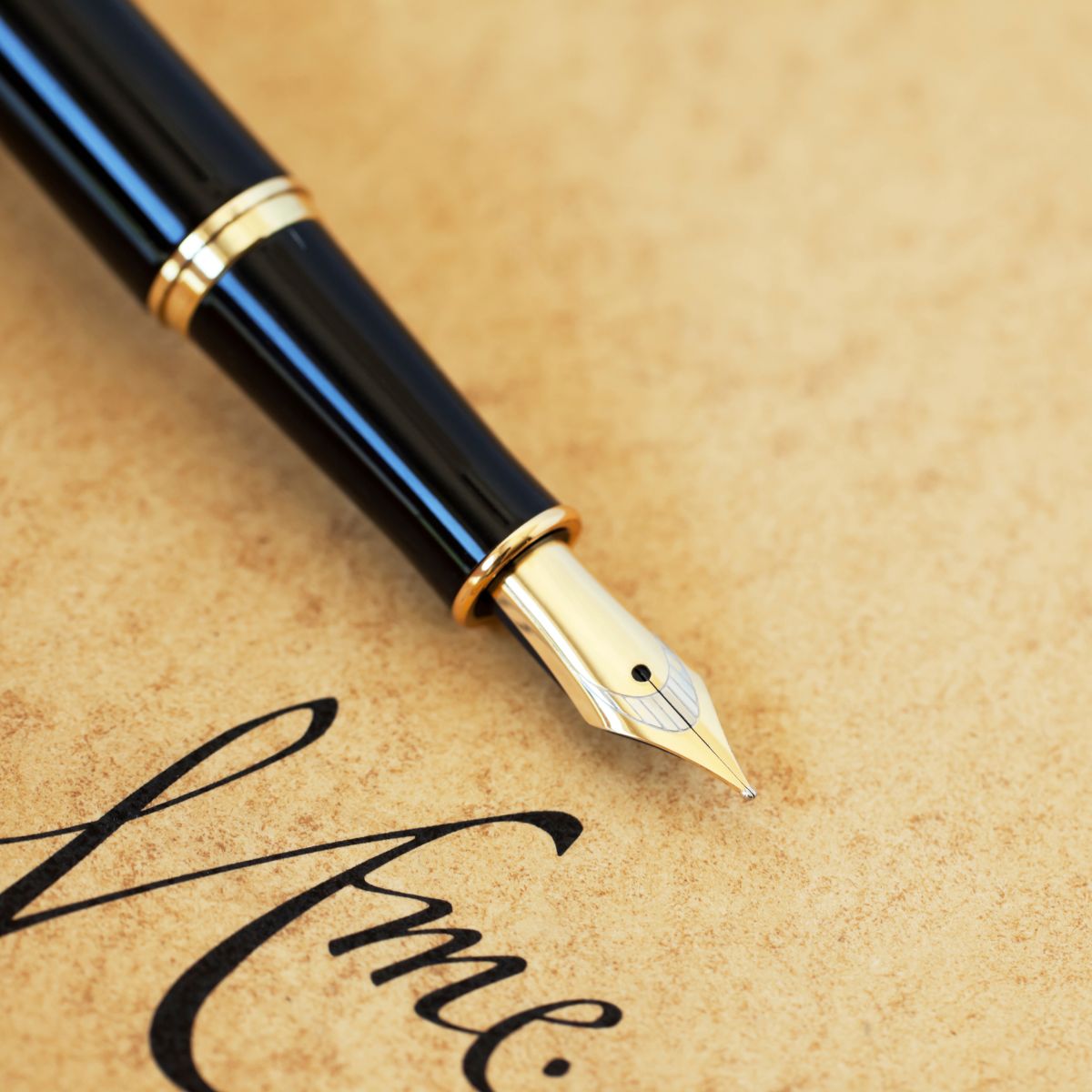 Close-up of an expensive pen with a gold nib resting on textured paper, next to elegant cursive writing.